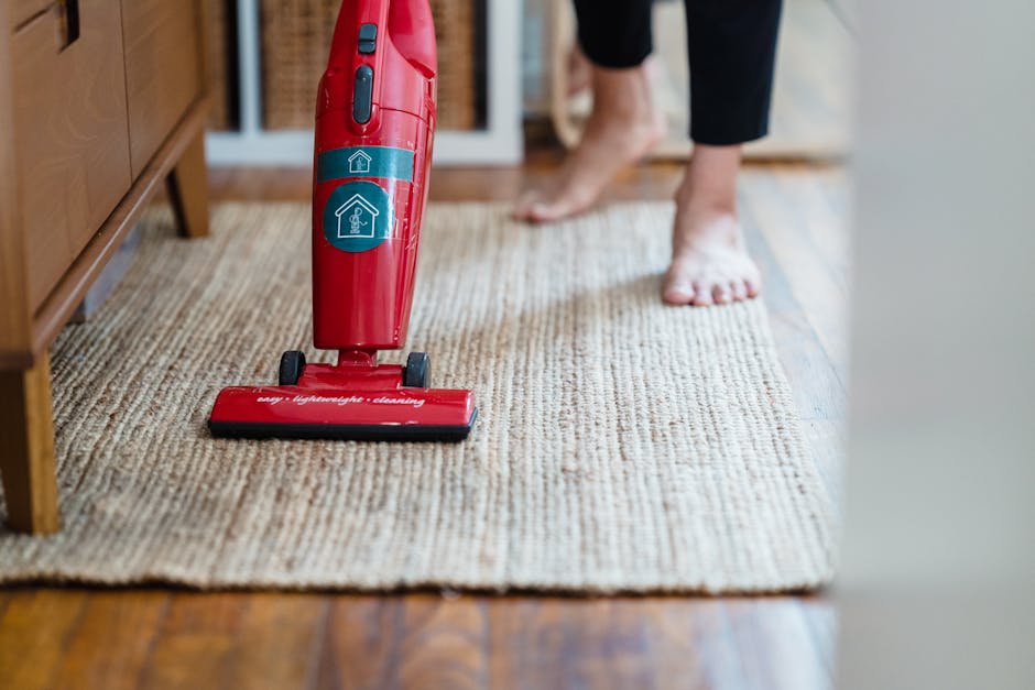 A person vacuuming a detailed patterned carpet in a well-lit room, using a black and silver vacuum cleaner with a long handle. The carpet features intricate floral designs in muted tones of green, beige, pink, and orange. The individual is wearing casual clothing, including dark jeans and white sneakers, and is standing upright while cleaning. The clean and shiny surface of the carpet suggests professional deep cleaning by Twickenham Carpet Cleaning, aligning with best hygiene and maintenance practices in residential settings, especially relevant to Richmond Council's carpet cleaning rules highlighted on the webpage.